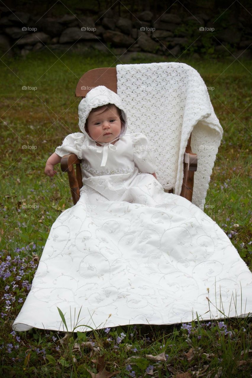 Baby in white wedding dress sitting on chair