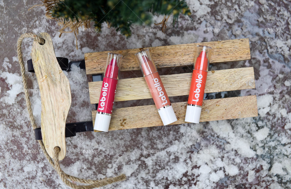 Row of Labello lip crayons on a mini wooden sled next to a pine tree in the snow