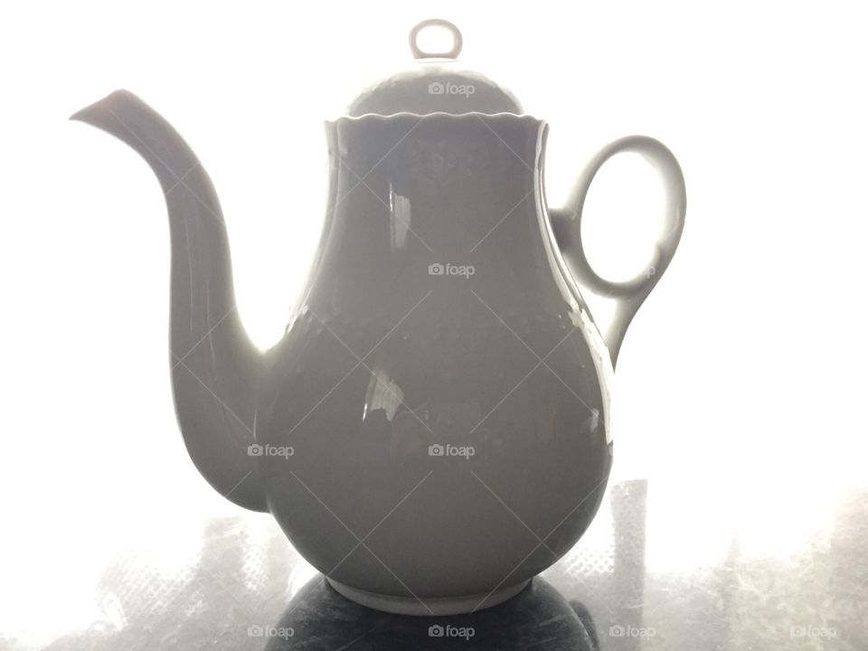 Backlit white porcelain teapot on reflective surface 