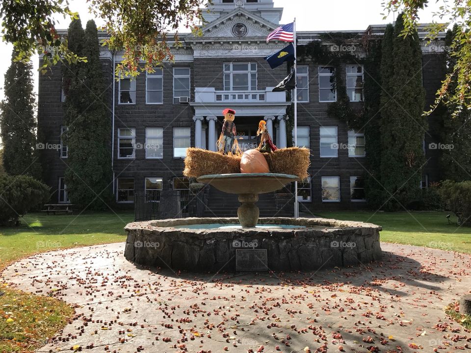 A pair of decorative scarecrows perched on hay bales with a pumpkin in the fountain at the old Crook County Courthouse in Prineville in Central Oregon on a beautiful fall day. 