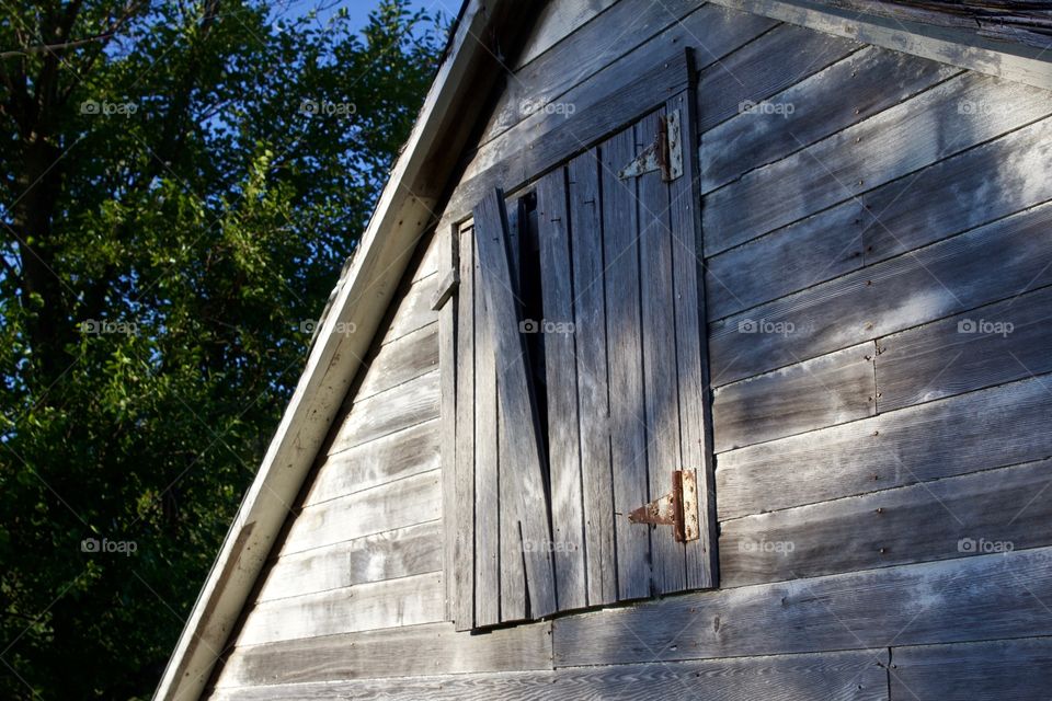 Isolated view of weathered wood siding and a hayloft door with rusty hinges in partial sunlight