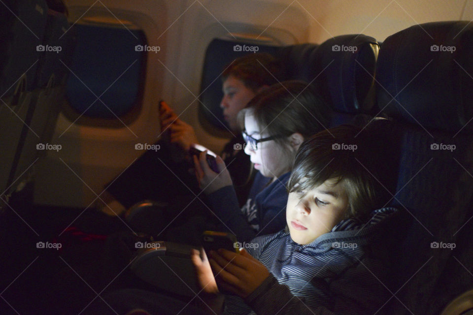 Three children on mobile devices on a plane