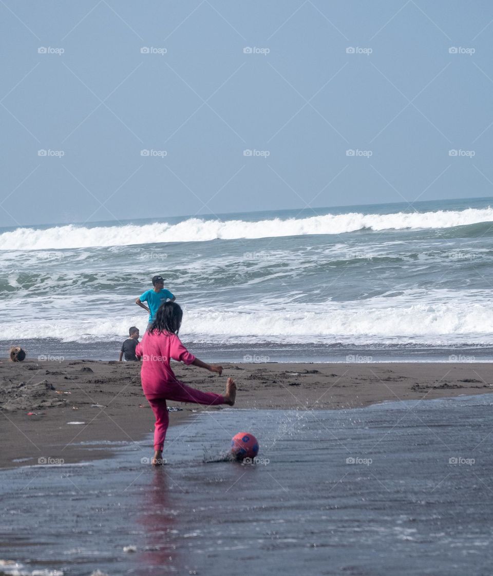 little girl playing football on the beach