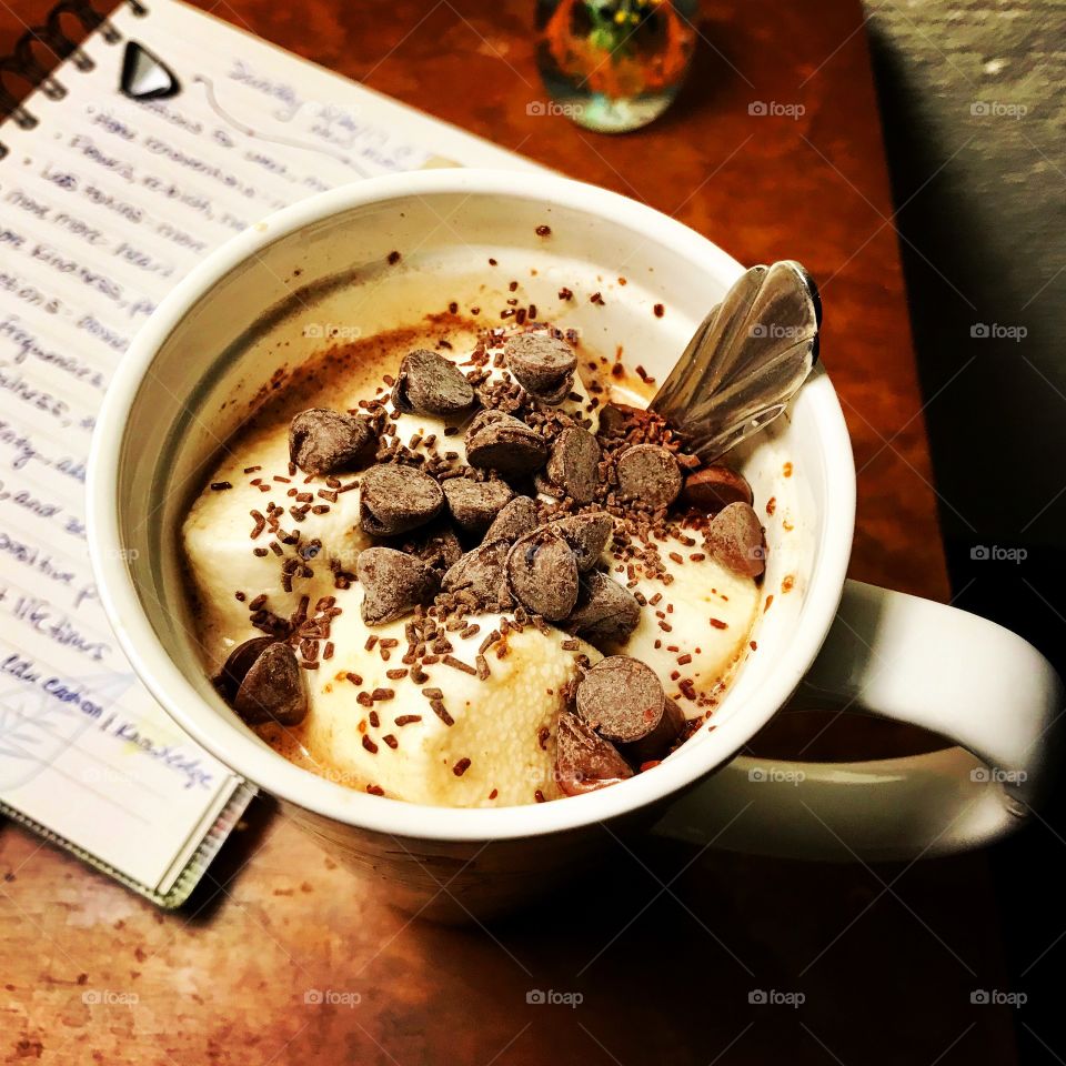 Hot cocoa with marshmallows and chocolate chips/sprinkles. Journal in the background. 
