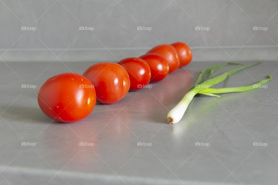 Fresh, bright, juicy vegetables and herbs for preparing salads and other vegetable dishes are on a gray, kitchen worktop.