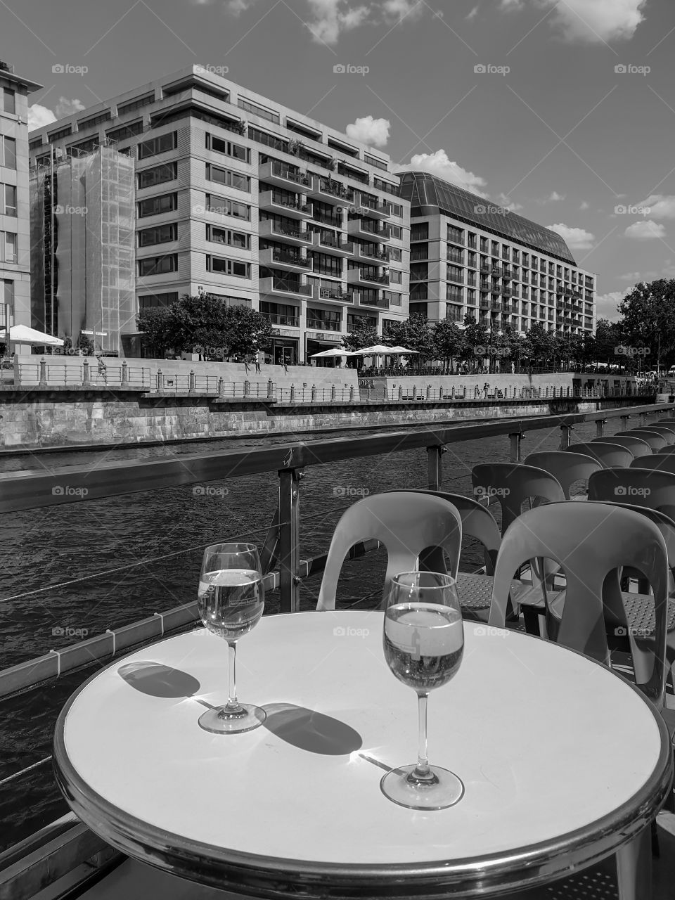 View from the pleasure river ship to the modern houses of the center of Berlin.  Monochrome cityscape with a pleasure boat with two glasses of white wine on the round table