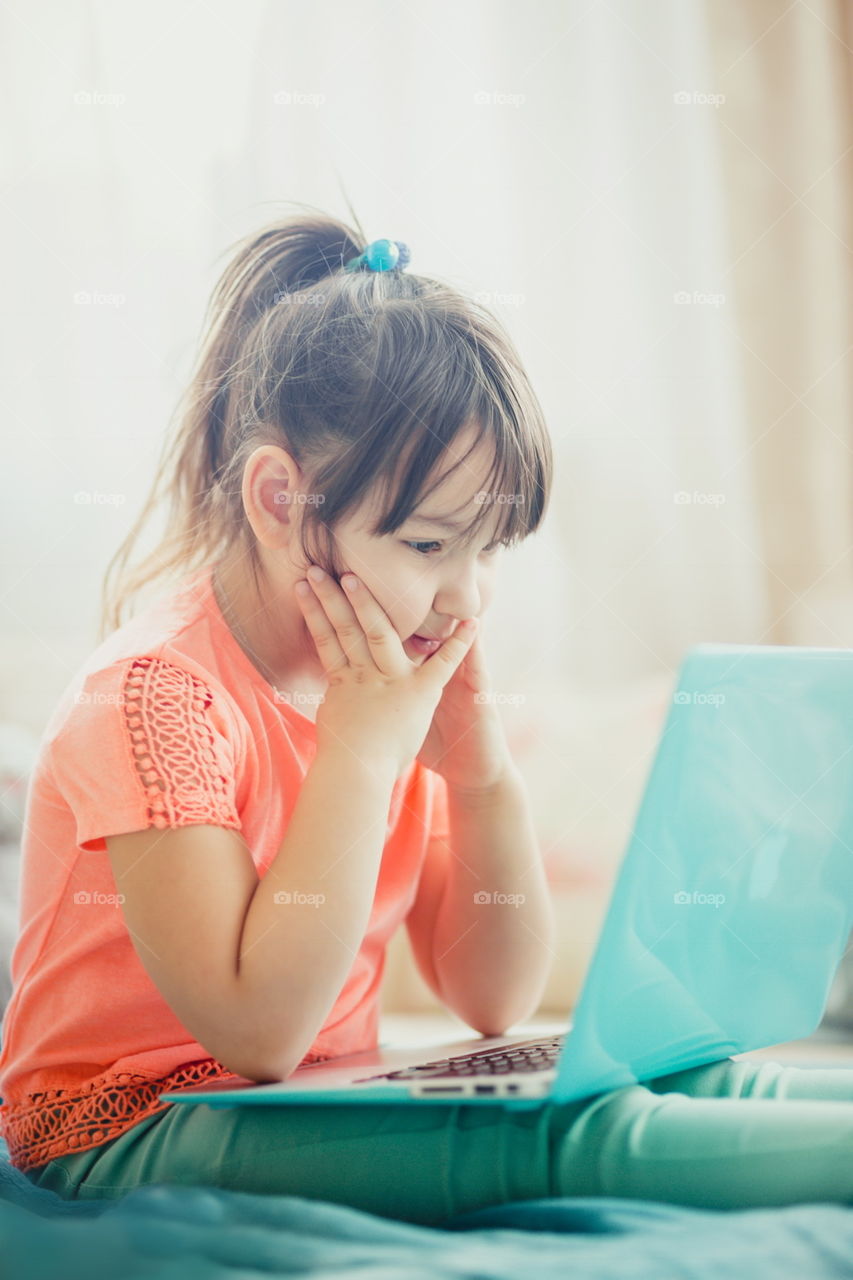 Little girl with gadgets(laptop and tablet) in the bed.