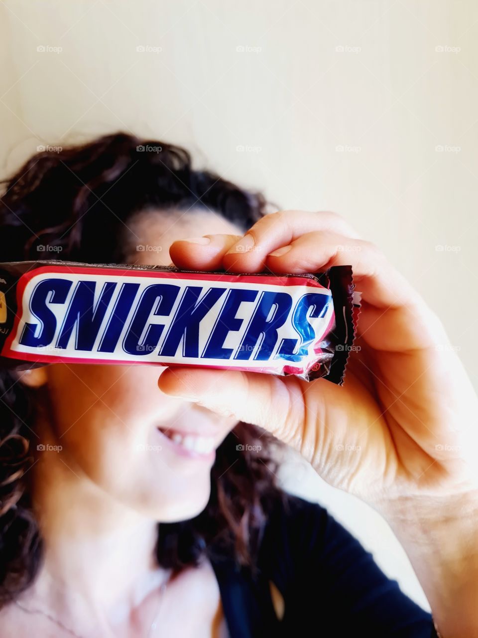 smiling woman covers her eyes with a pack of snickers