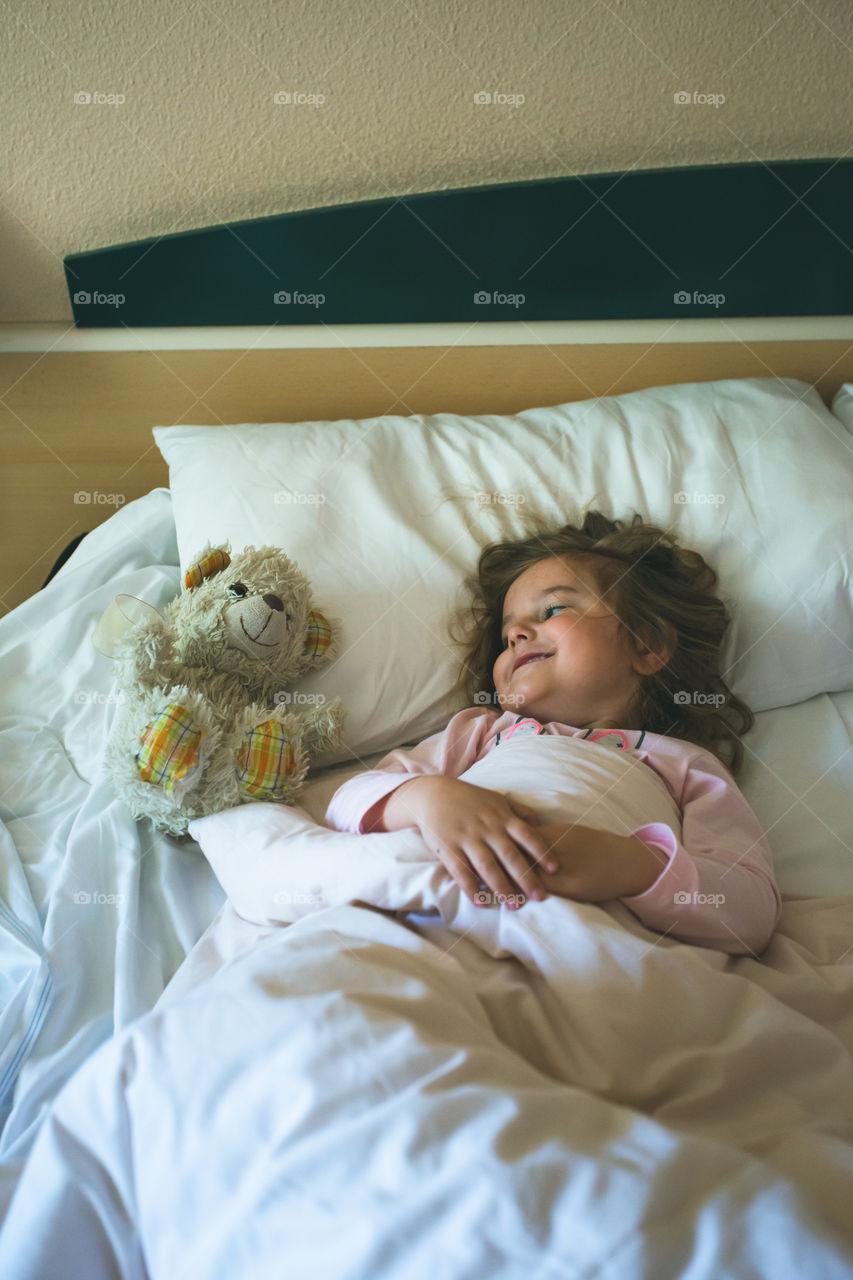 Little girl lying in a bed with teddy bear at the morning