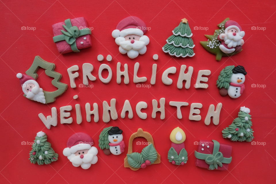 Creative german Merry Christmas, Fröhliche Weihnachten, with wooden letters and marzipan Christmas symbols over red color background