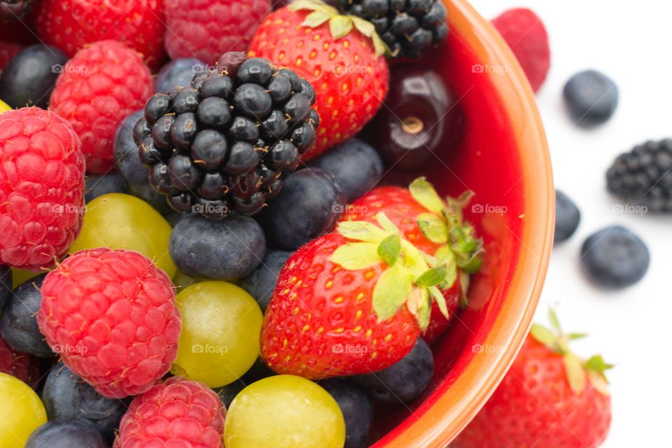 Ceramic bowl full of mixed forest fruits (blueberries, raspberries, blackberries and strawberries), cherries and grapes. White background