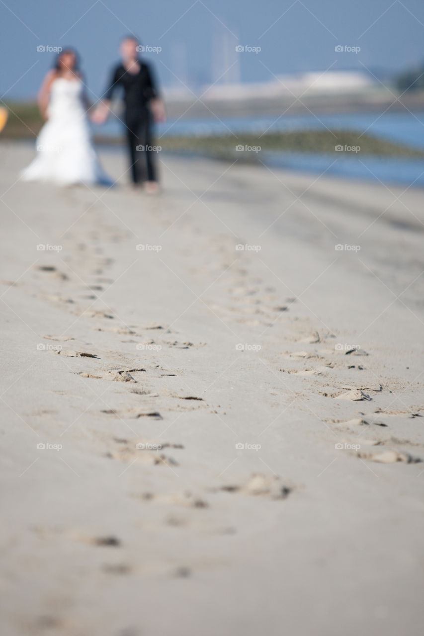 Out of focus newly wed couple walking on the beach in the distance showing their footsteps in  focus