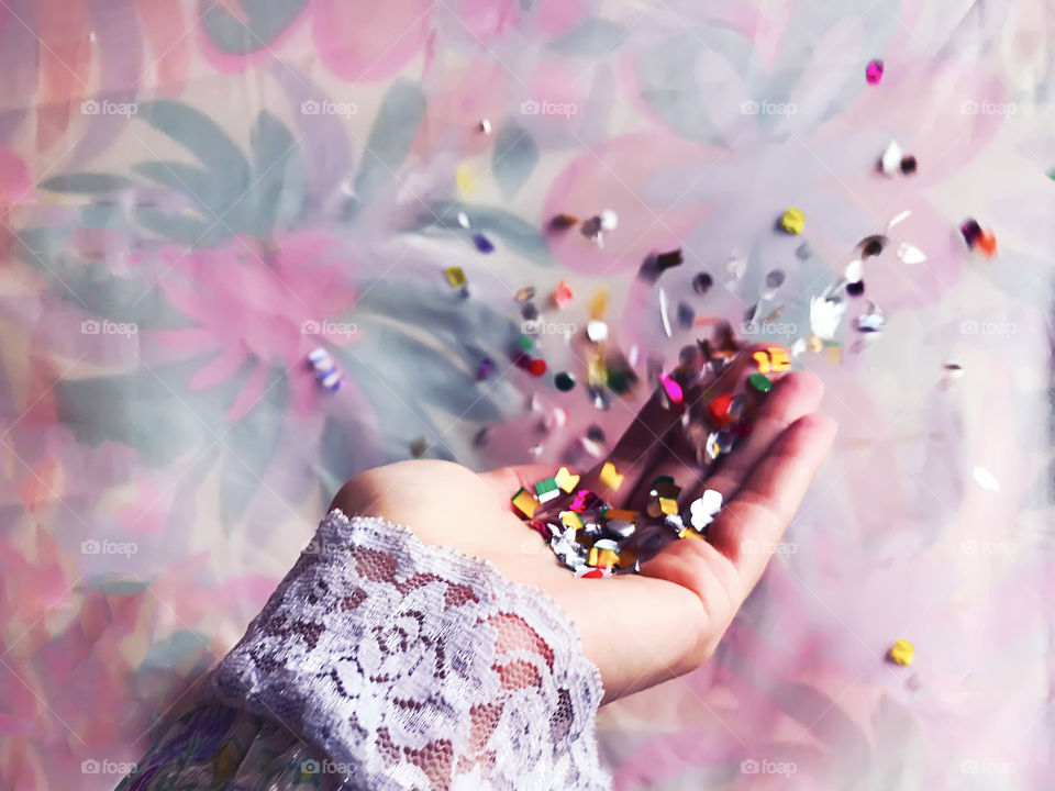 Blowing colorful confetti out of the female hand in front of colorful pastel background 