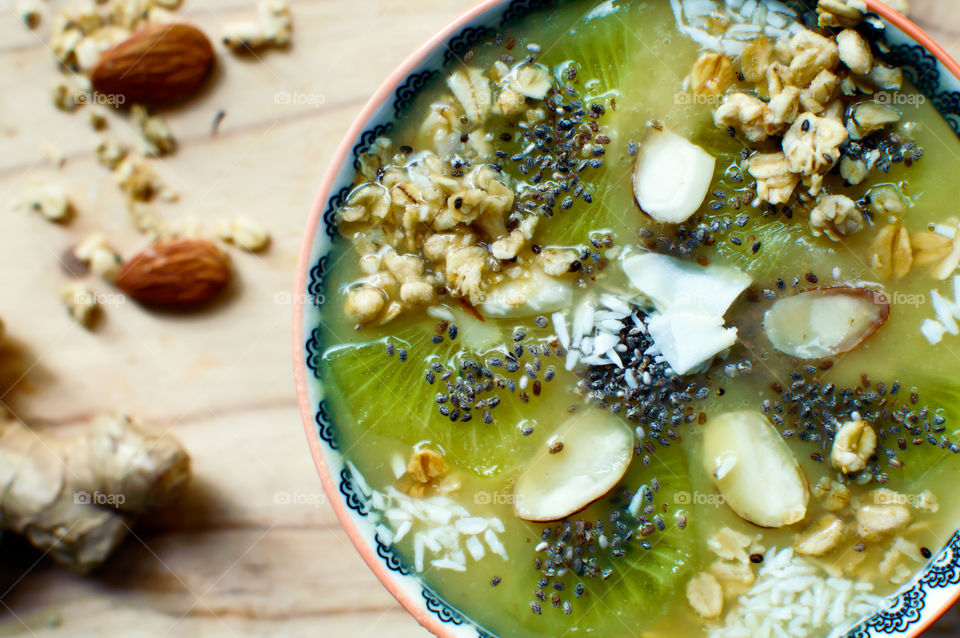 Close-up fresh healthy fruit smoothie bowl  with ginger, chia seed,  almond, kiwi, coconut and oatmeal in mandala design elevated view  green and white colors 