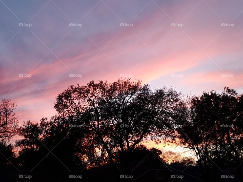 Watercolor wispy clouds at sunset in shades of pink clouds against shades of purple in the normally blue sky.