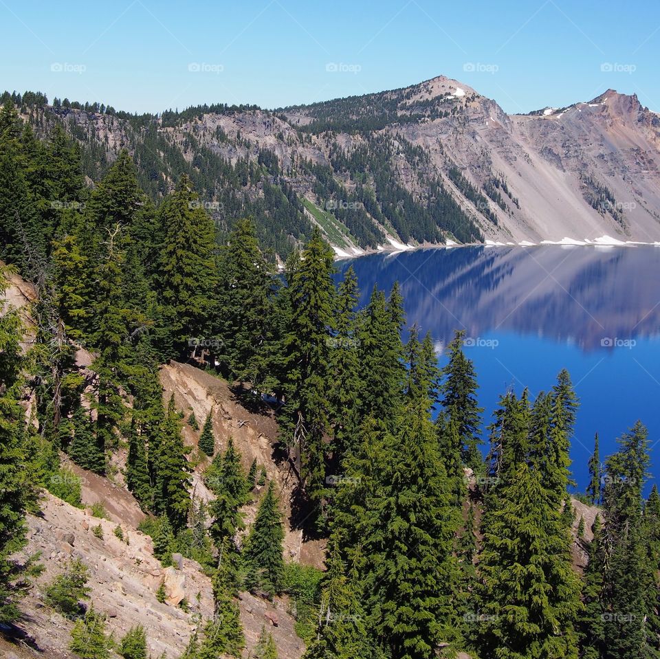 The jagged rim reflecting into the rich blue waters of Crater Lake in Southern Oregon on a beautiful summer morning with perfect clear blue skies.