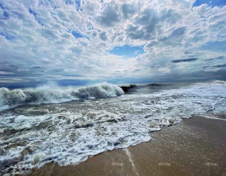 Waves roll onto the sand underneath a cloud filled sky at the beach 