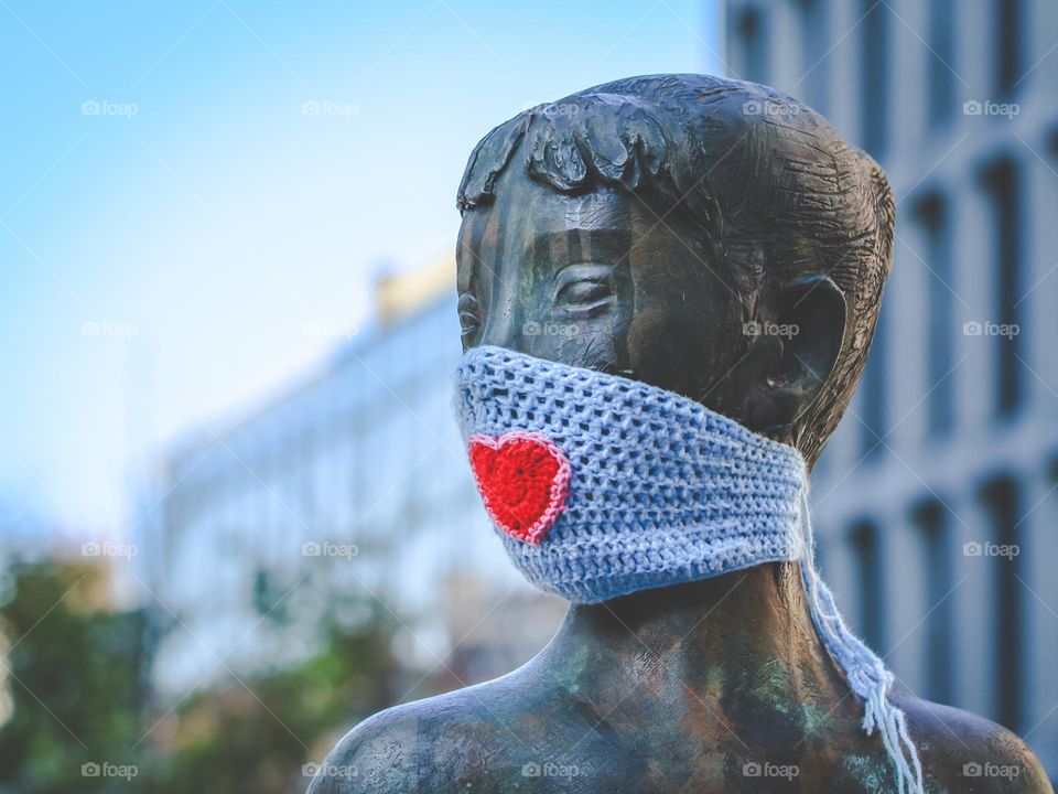 Beautiful portrait of a monument of a girl with a knitted homemade mask with a red heart on a summer day in the city of Brussels near the European Parliament, vtd side close-up. Belgium monuments concept,coronavirus,Valentine's day.