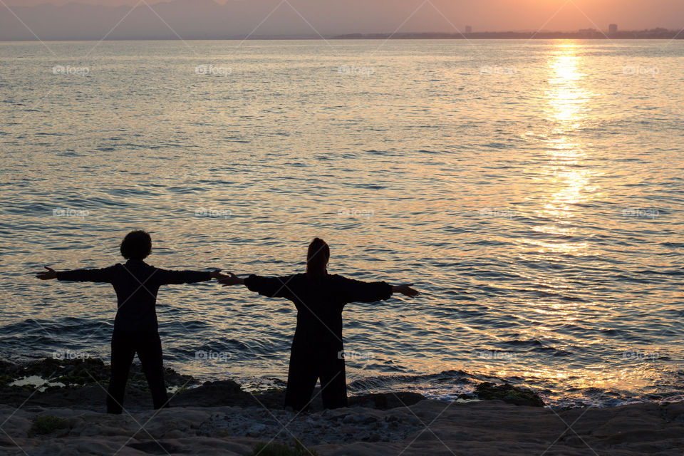 Two women practice yoga facing the sea.