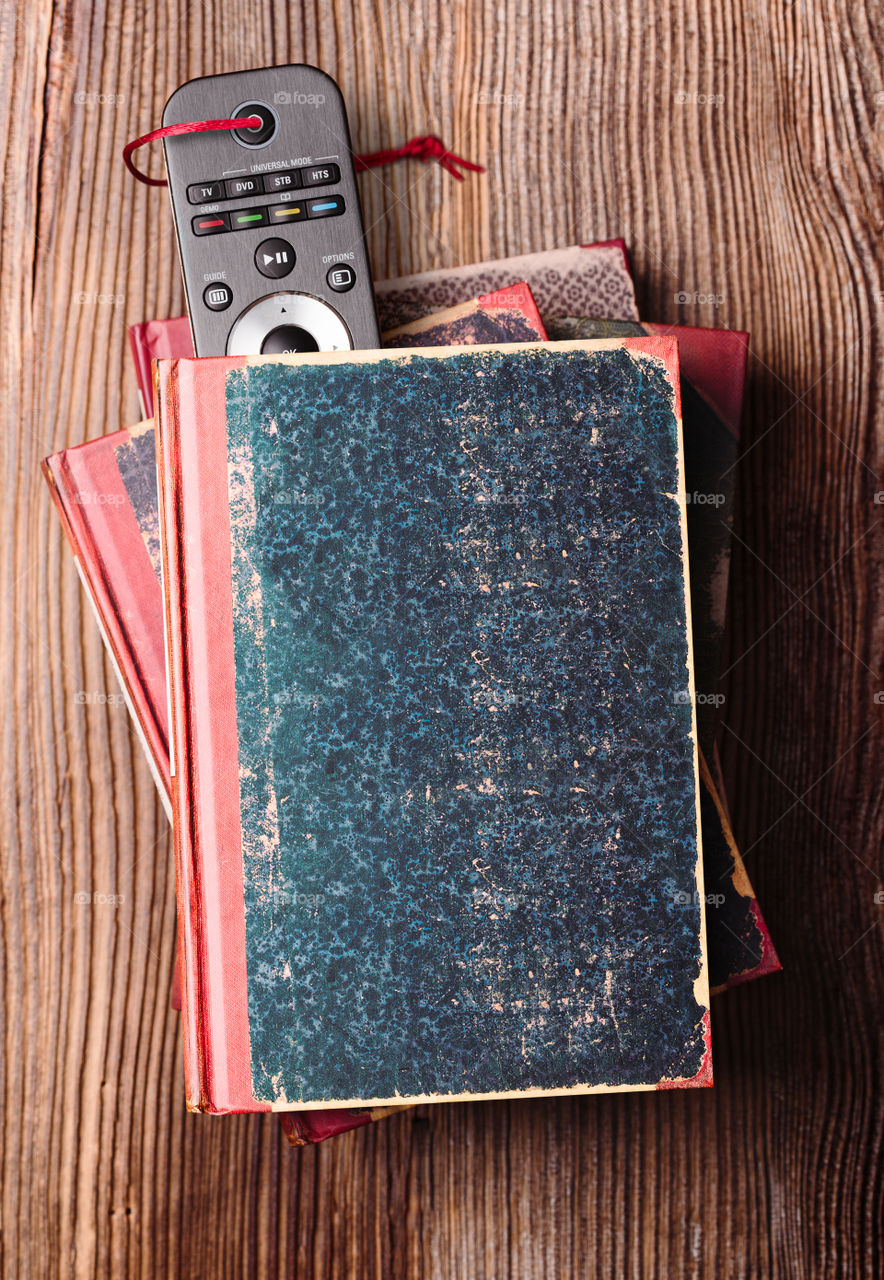 Stack a few books on wooden table with bookmark in shape of tv remote inserted in one book