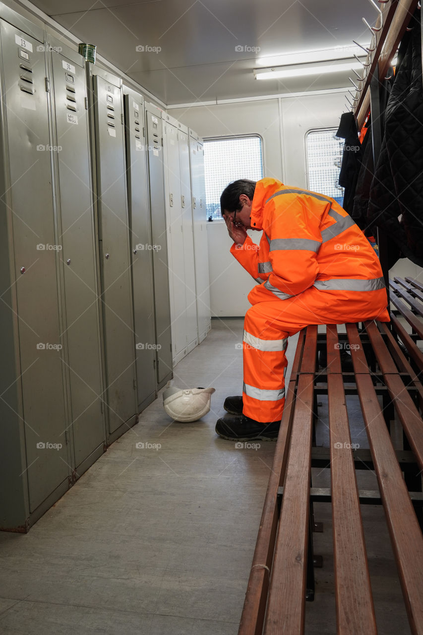 A construction or railway worker sitting alone in a locker room feeling grief sadness and loss in a mental health at work concept with copy space