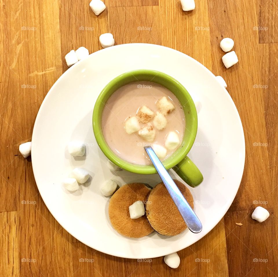 Warm hot cocoa in a green mug with mini marshmallows and cookies. Keeping warm this winter 