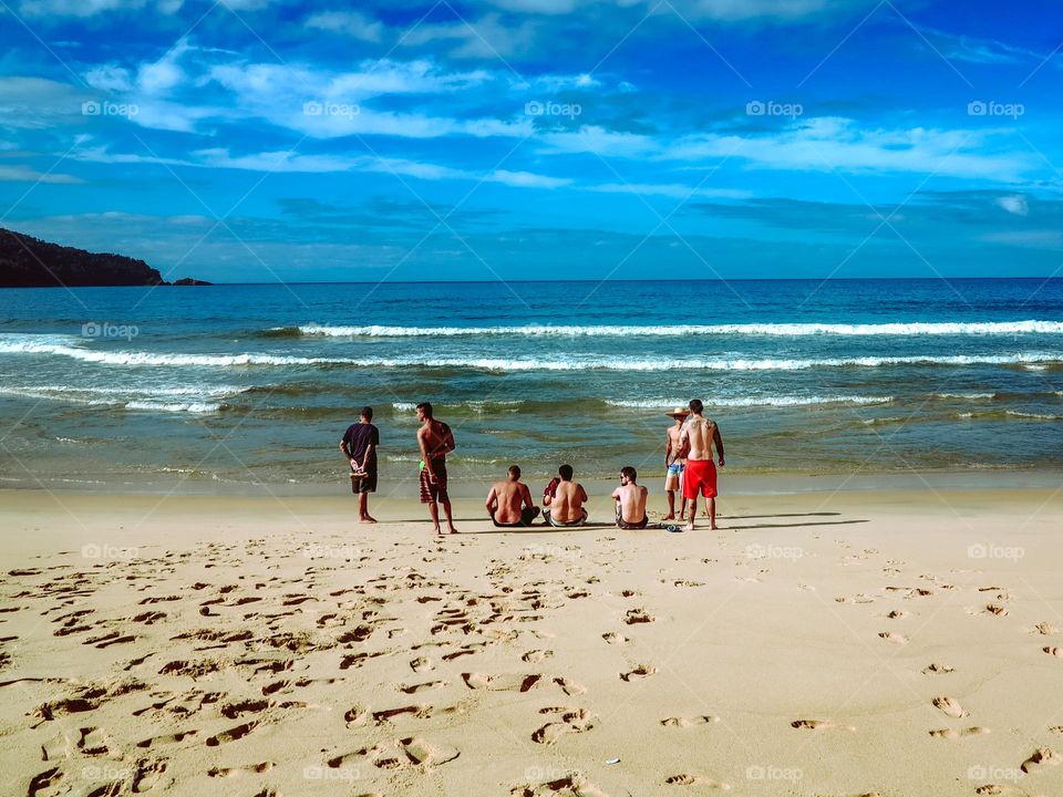 Sunrise at the Atlantic Ocean, beautiful shot of 7 men at the beach. Blue Ocean and blue sky at Praia do Sono, Brasil.