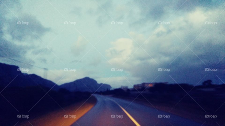 Picture taken from a moving car on a coast road in South Africa on a stormy winters evening and a orange sunset from behind