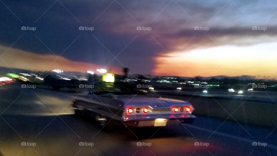 highway to hell. large smoke cloud from fire in background as classic car speeds down 91 freeway west near orange county