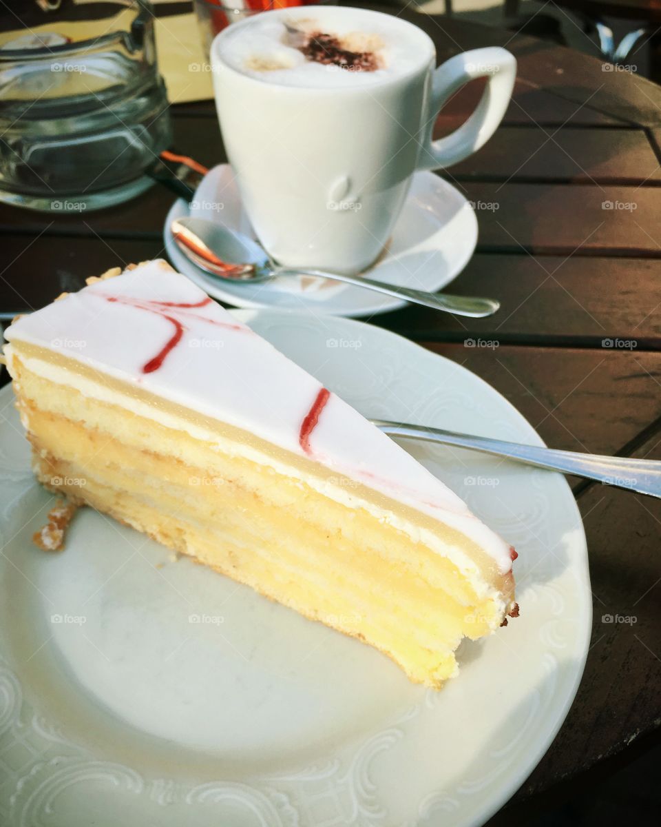 A cup of cappuccino and lemon cake on a wooden table