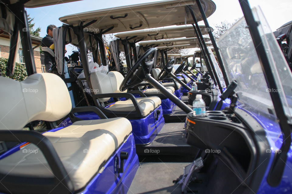 A long line of empty golf carts waits for passengers at a golf course