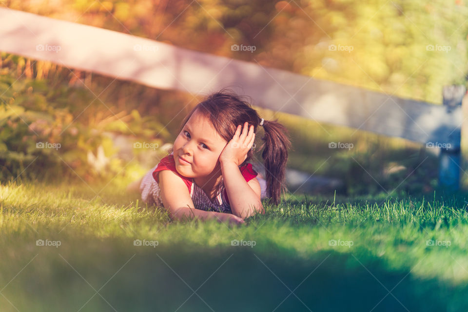 Portrait of cute little girl lying on green grass