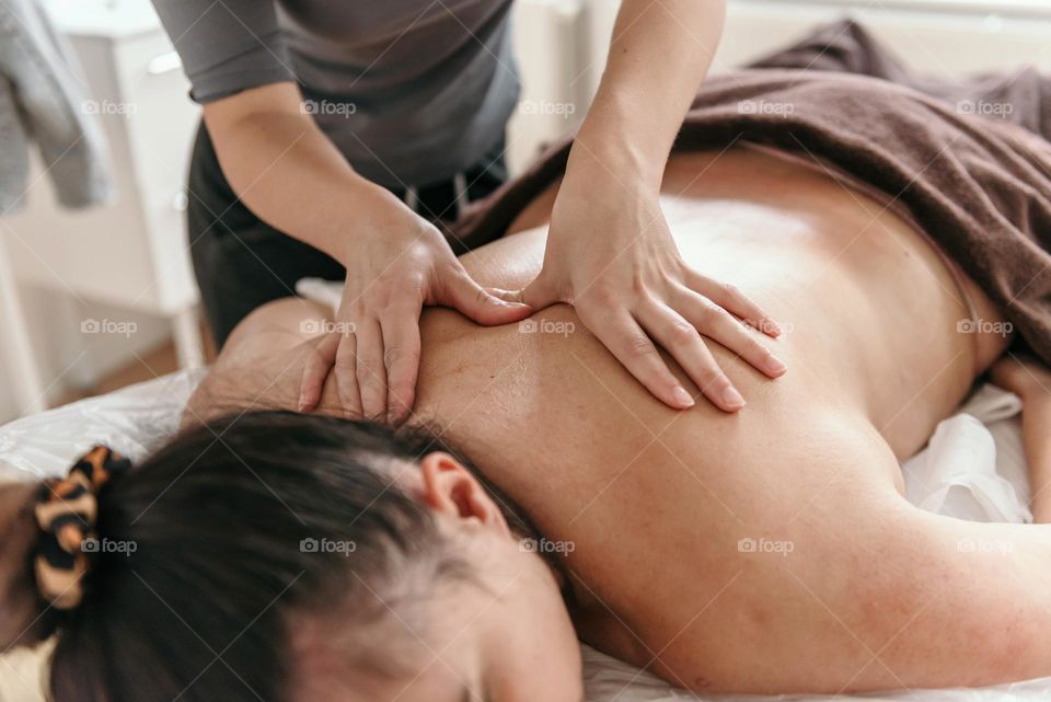 Masseuse doing back massage on young woman