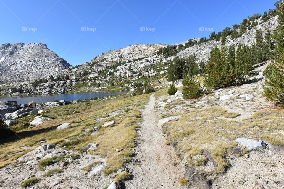 A dirt trail leads the way past a wilderness lake