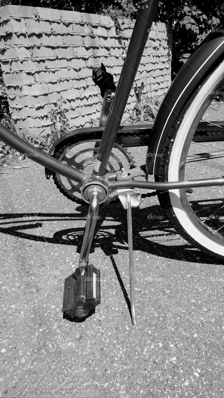 lonely bike pedal and kick stand in black and white with a brick background bike chain and white wheel well