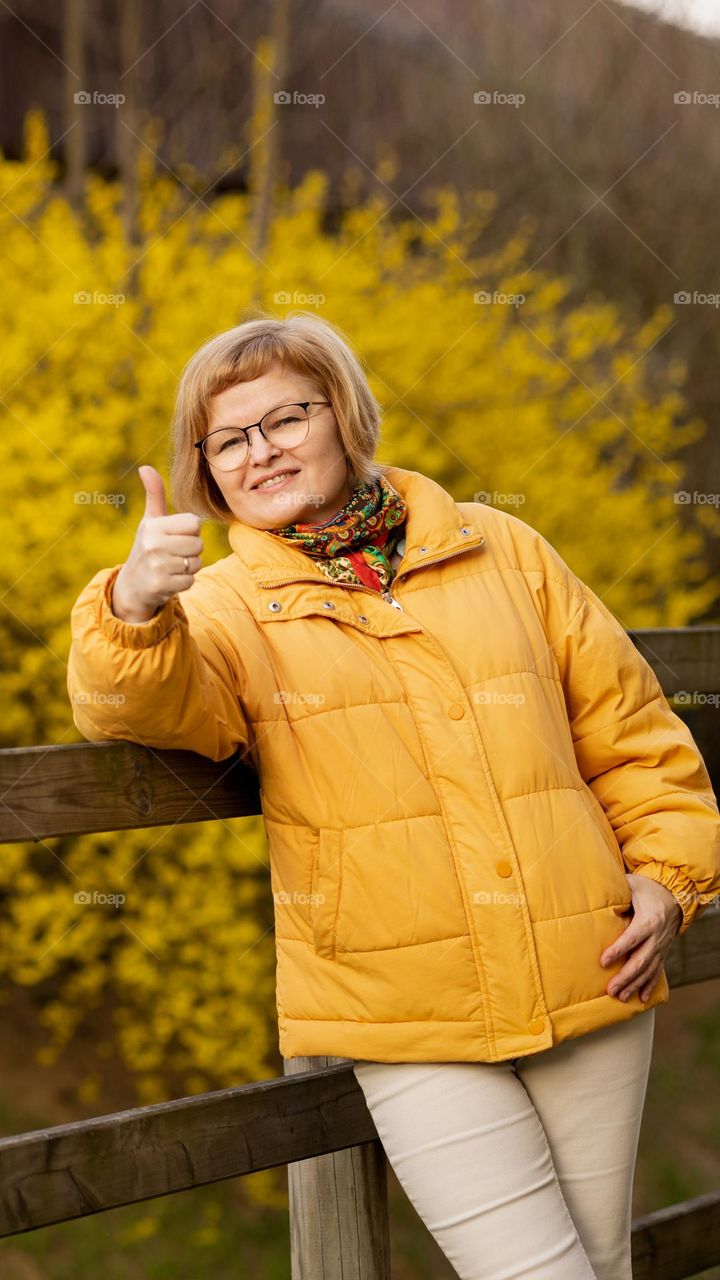 A woman in a yellow jacket on the background of blooming forsythia.