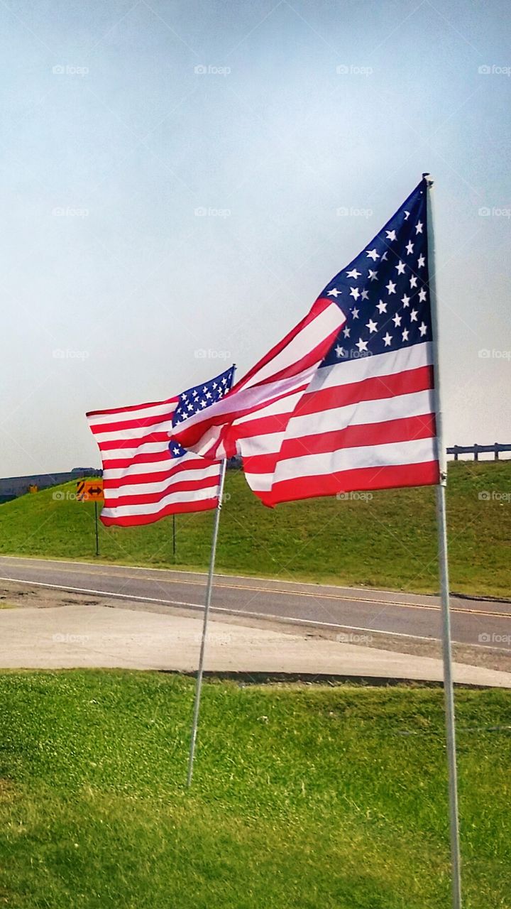 Two American flags waving in the breeze along a highway