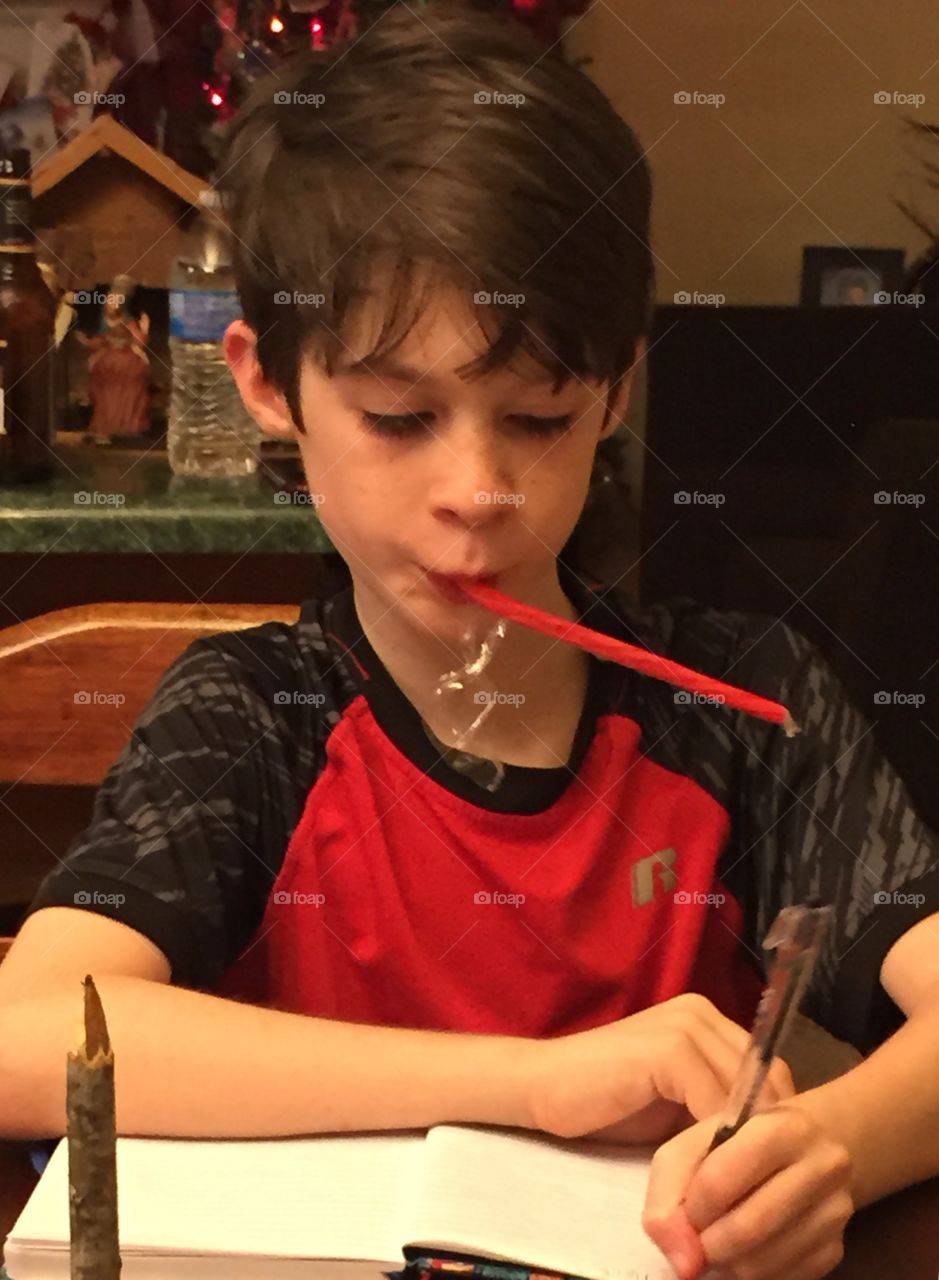 Young 8 year old boy sucking on a strawberry colored candy cane and writing in his journal Christmas night.