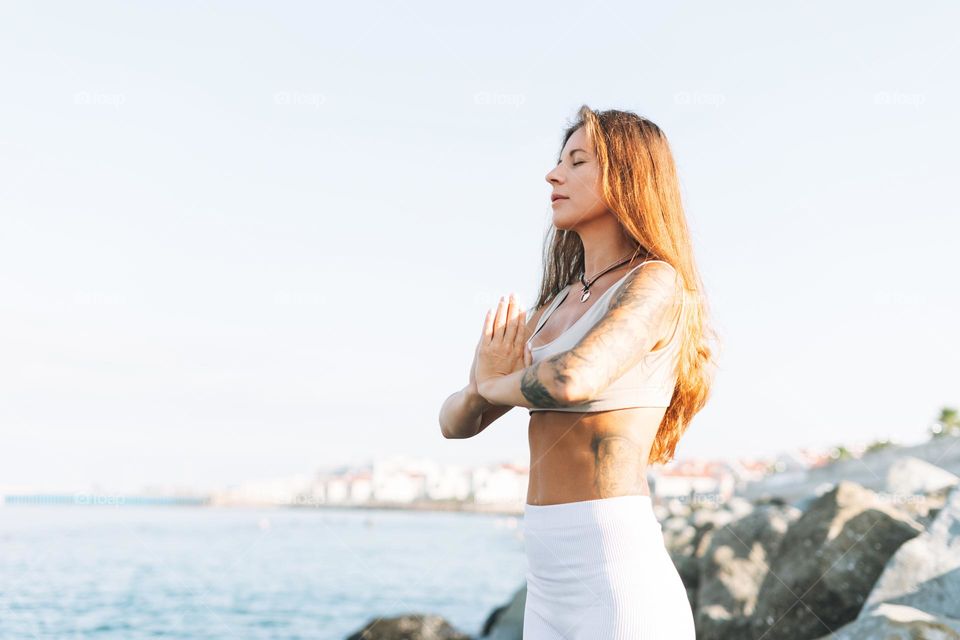 Crop photo of young fit beautiful woman with long hair in white sport clothes practice yoga and enjoy life on the sea beach, mental and phisical health