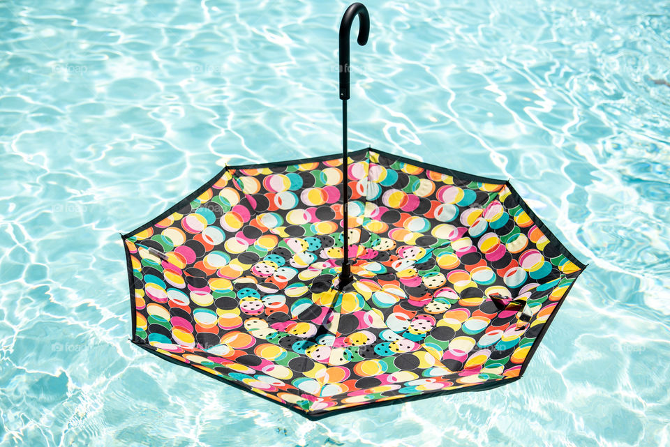 Colorful spotted umbrella floating on top of an outdoor swimming pool