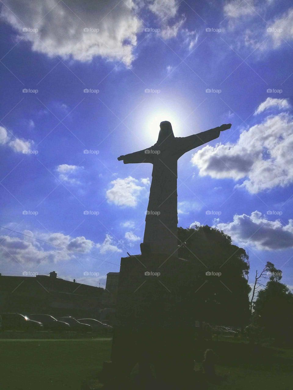 imitación de la estatua del Cristo Redentor emplazada en una plaza de barrio, destacándose su silueta en un cielo muy azul, soleado y con algunas nubes.