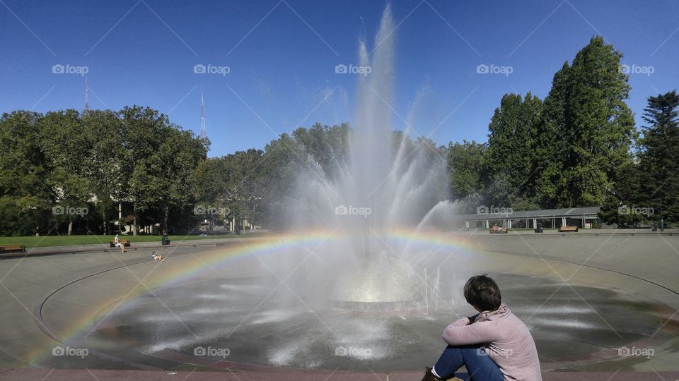 Woman sitting by a fountain  with a rainbow