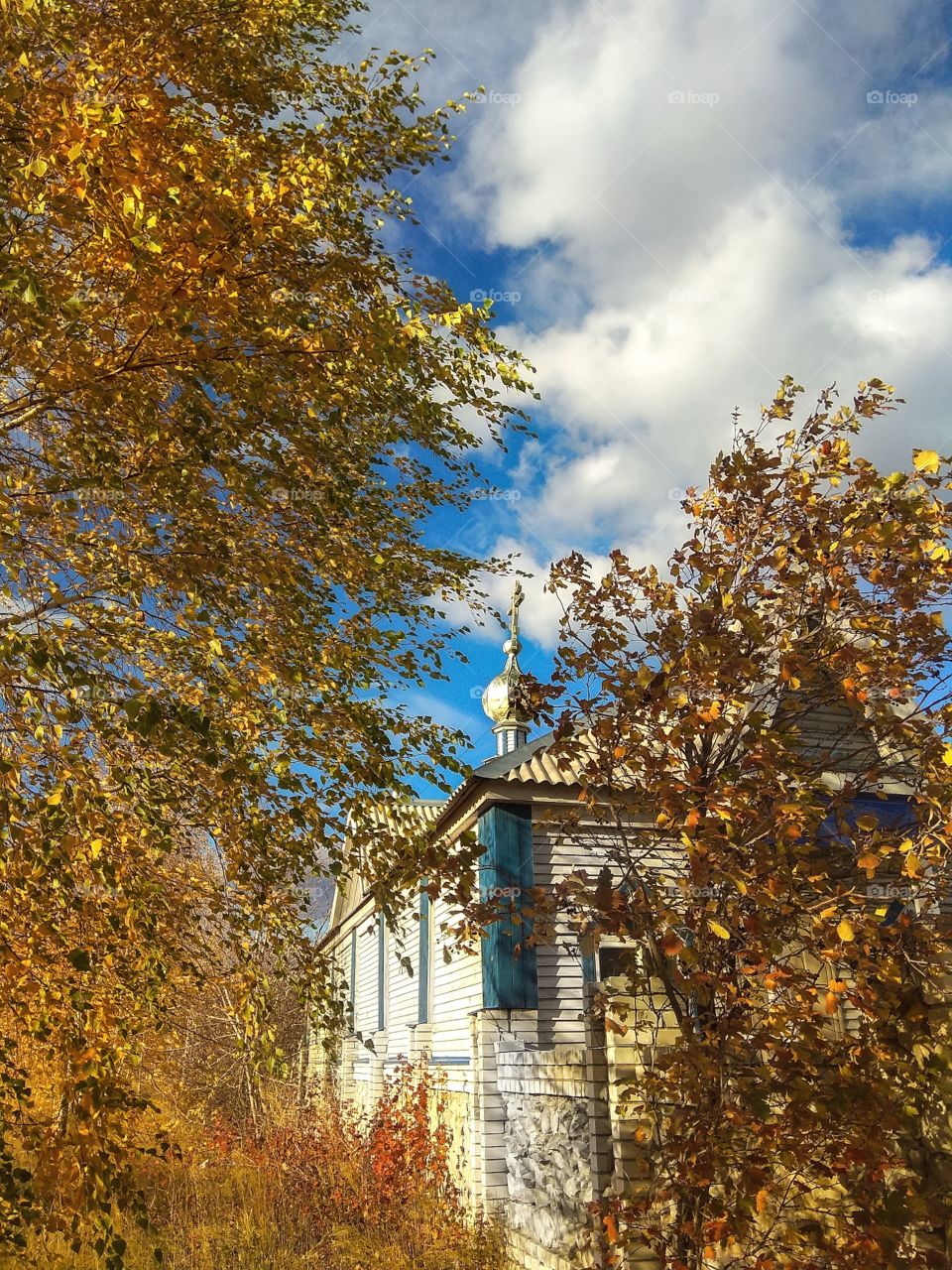 Chapel of St. Nicholas Church (Russia, Ulyanovsk) and golden leafy trees under a beautiful cloudy sky on a sunny autumn day