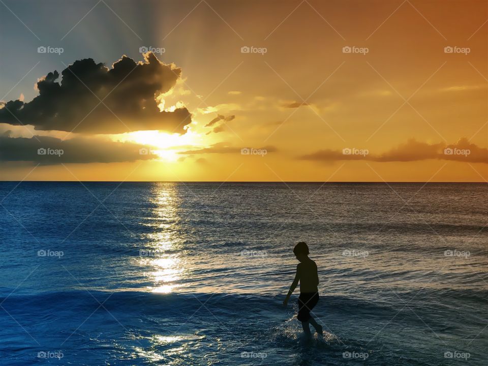 Small boy at sunset playing in the ocean in the light of a golden sun.