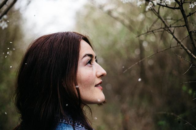 Young beautiful woman, admiring the blossomed trees while taking a walk in the forest, on a beautiful spring day.