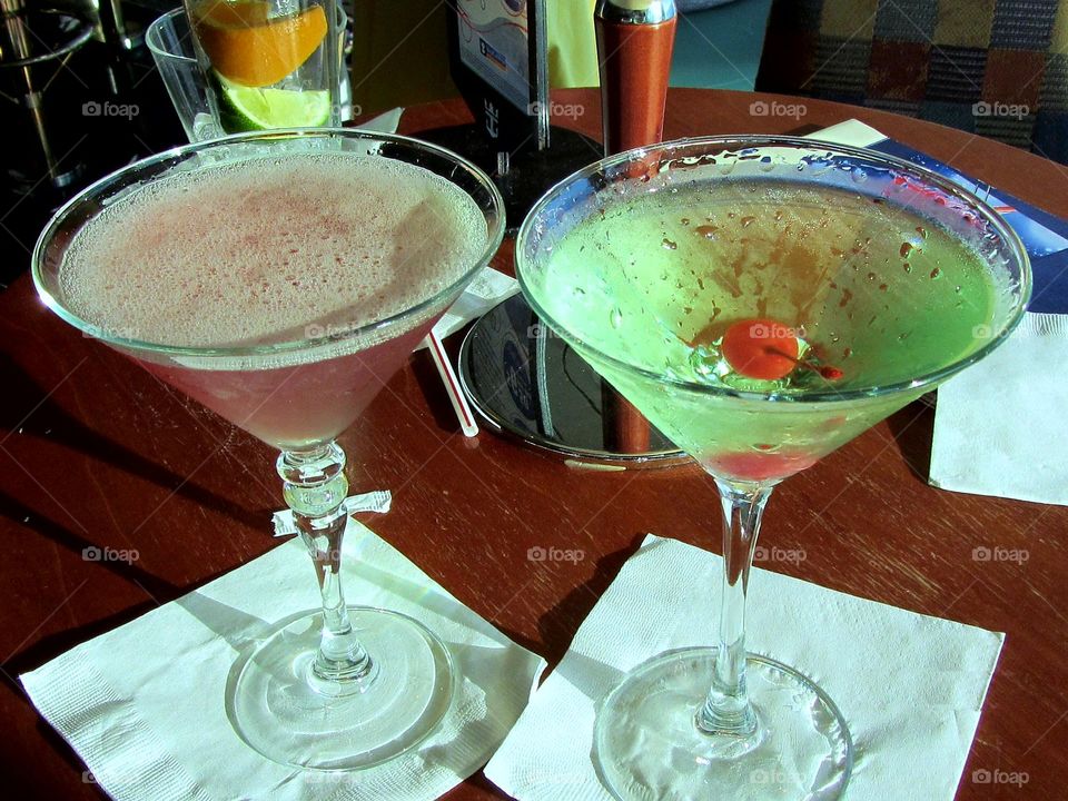 Pick & green martinis sitting on napkins, one has a cherry in it. Green Apple martini, Pink House Martini in martini glasses🍸🍸!