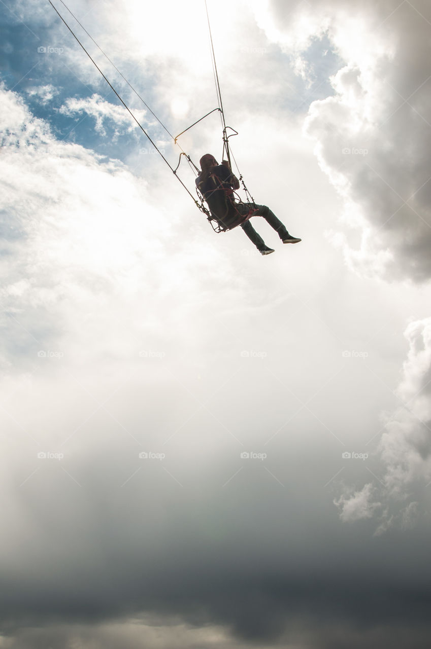 A man on a swing with the sky and the clouds in the background 