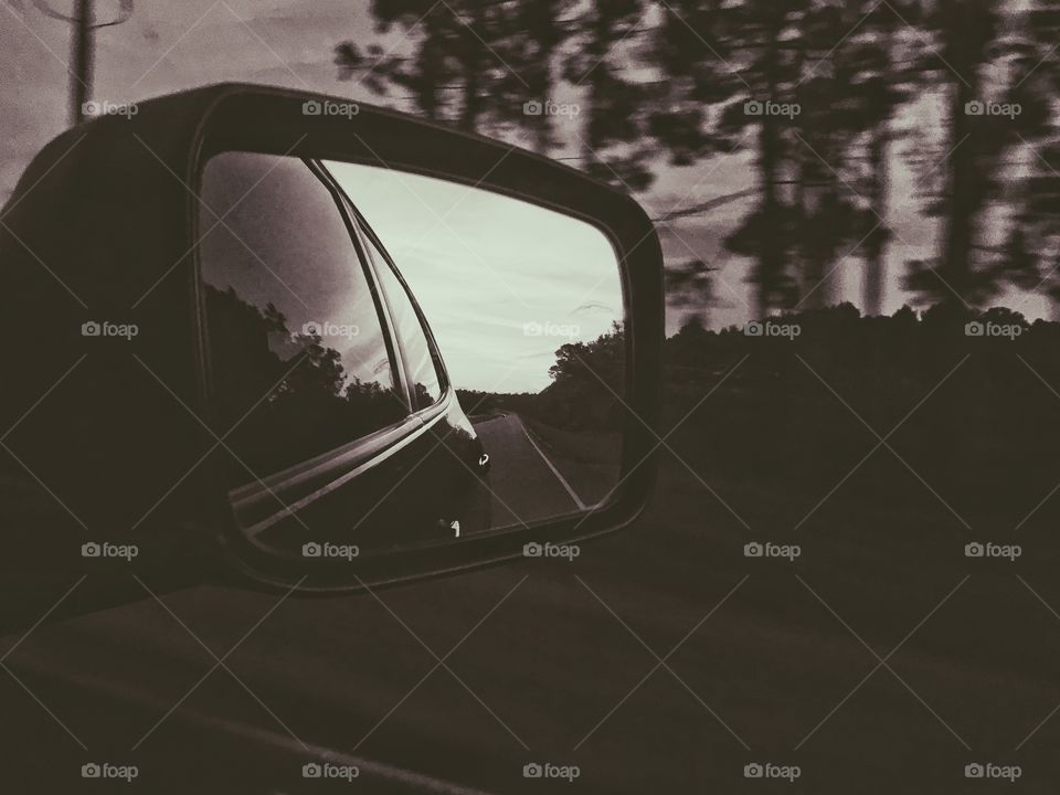 Black and white photo of the side car mirror driving down a highway. 