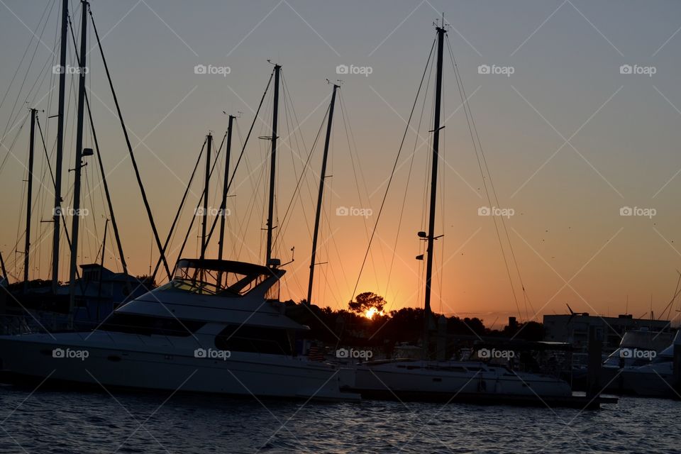The sun setting behind several sailboat masts on a river