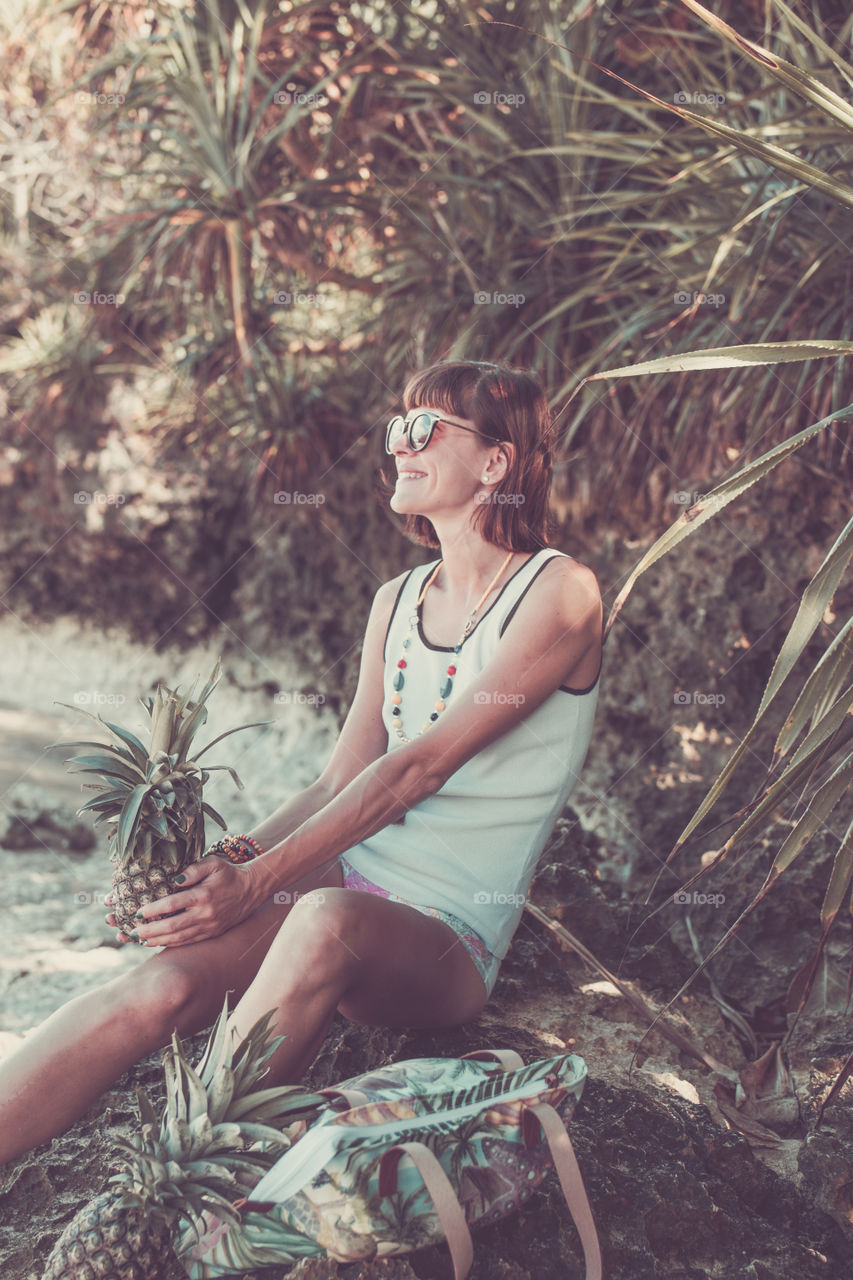 A girl in the tropics is photographed with pineapple.